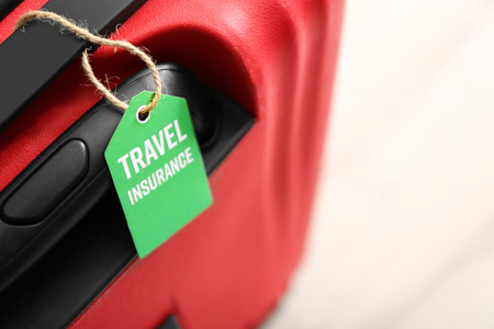 Red suitcase with label, closeup. TRAVEL INSURANCE conceptの写真素材