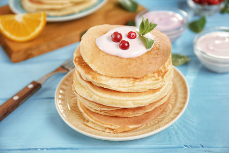 Plate with delicious pancakes, yogurt and cranberry on blue table