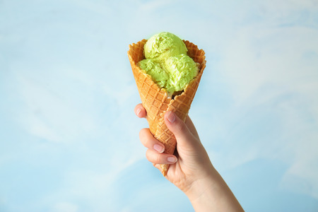 Female hand holding waffle cone with tasty ice cream on light background