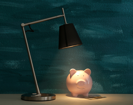 Cute pink piggy bank on illuminated surface under lampの写真素材