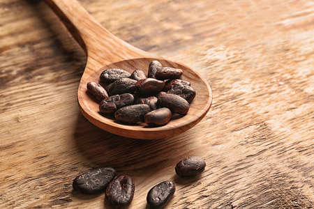Spoon with aromatic cocoa beans on wooden tableの写真素材
