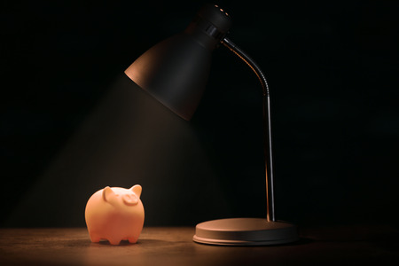 Cute piggy bank on illuminated surface under lampの写真素材