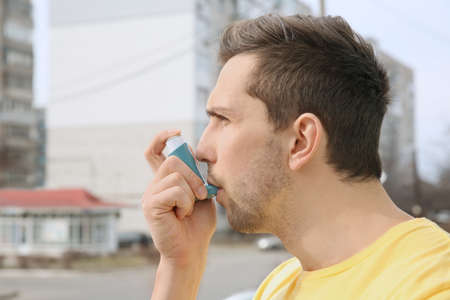 Young man using inhaler during asthmatic attack outdoorsの写真素材