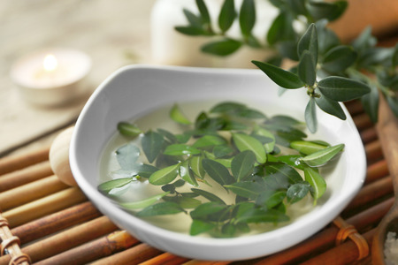 Bowl with water and green leaves on bamboo matの写真素材