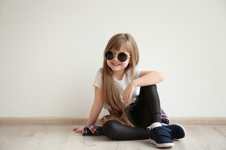 Cute little girl sitting on floor against light wall background. Fashion conceptの写真素材