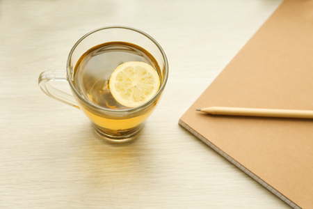 Cup of hot tea, notebook and pencil on wooden tableの写真素材
