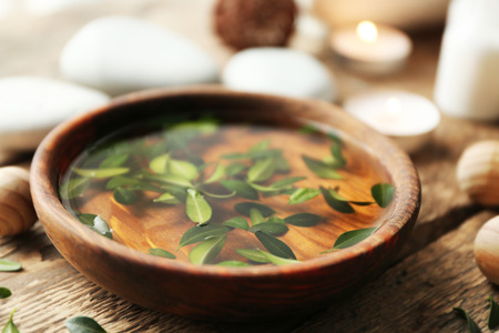 Bowl with water and green leaves on wooden table, closeupの写真素材