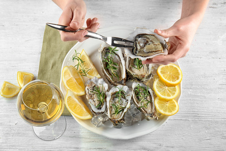 Woman eating tasty fresh oysters with sliced lemon and rosemary on plate. Aphrodisiac food for...
