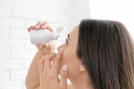 Young woman with bottle of solution for contact lenses, closeup view