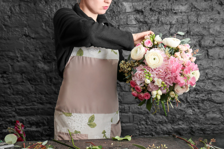 Female florist creating beautiful bouquet in flower shop on black brick wall backgroundの写真素材