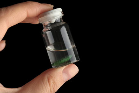 Woman holding glass bottle with contact lens on dark backgroundの写真素材