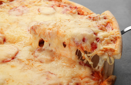 Slice of delicious pizza with melted cheese on shovel over wooden boardの写真素材