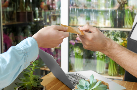 Young handsome florist receiving discount card from regular customer in flower shop, close upの写真素材