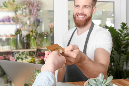 Young handsome florist receiving discount card from regular customer in flower shopの写真素材