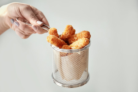Female hand holding metal basket with cheese sticks on light backgroundの写真素材