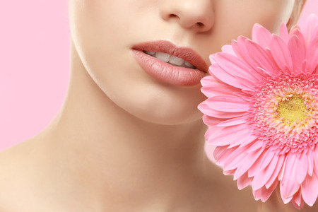 Closeup view of beautiful young woman with natural lips makeup and flower on color backgroundの写真素材