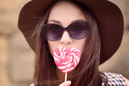 Beautiful young woman hiding lips behind tasty lollipop on blurred backgroundの写真素材