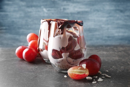 Delicious yogurt parfait with chocolate sauce in glasses and grapes on tableの写真素材