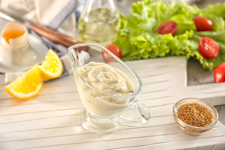 Delicious mayonnaise in gravy boat with ingredients on kitchen tableの写真素材