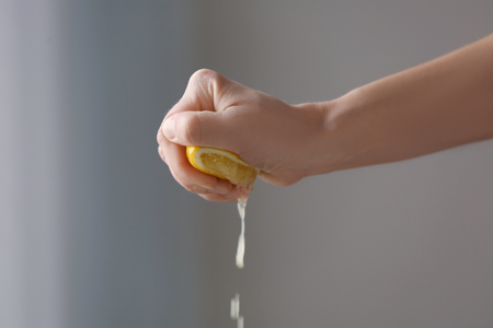 Female hand squeezing half of lemon on blurred backgroundの写真素材