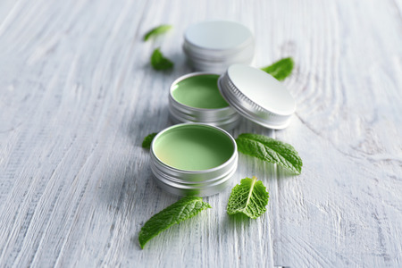 Containers with lemon balm salve and leaves on wooden table