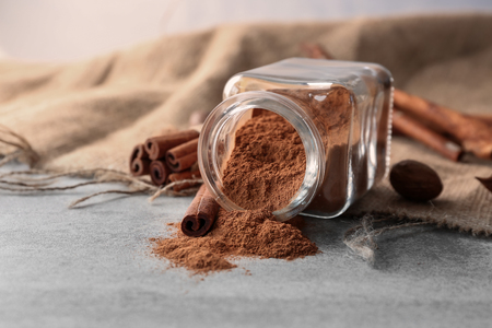 Glass jar with powdered cinnamon and sticks on light tableの写真素材
