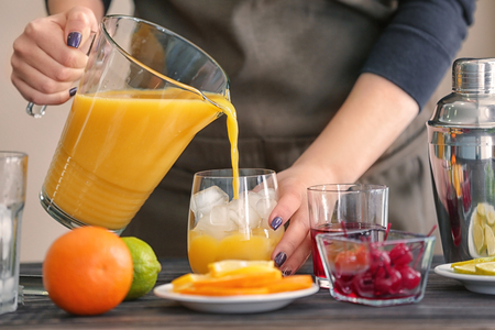 Woman preparing Tequila Sunrise cocktail on kitchen tableの写真素材