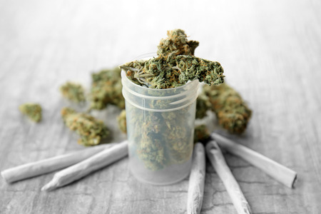Weed buds in plastic container with cigarettes on grey background