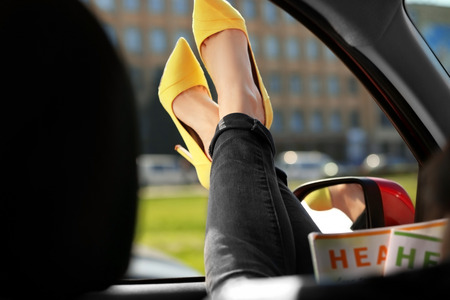Young woman with slim legs in high heels relaxing in carの写真素材