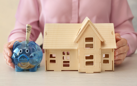 Young woman sitting at table with model of house and piggy bank. Savings conceptの写真素材