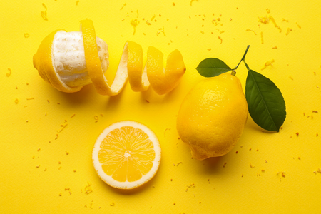 Delicious sliced and peeled lemons with green leaves on color background