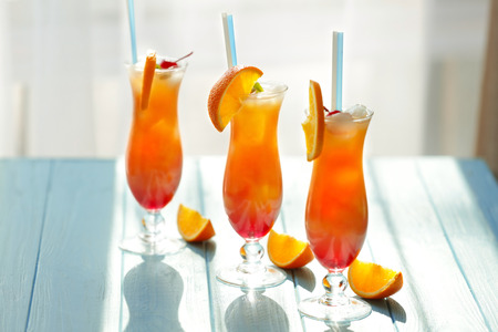 Glasses of Tequila Sunrise cocktail with orange slices on blue table
