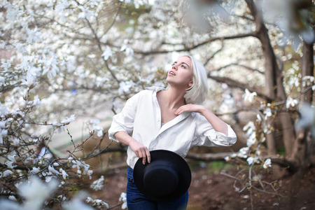 Young blonde girl near blooming magnolia tree on blurred background