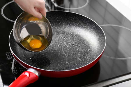 Woman pouring egg from bowl into frying panの写真素材