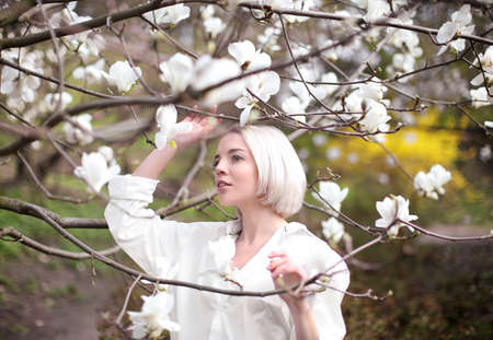 Young blonde girl near blooming magnolia tree on blurred background