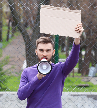 Protesting young man holding piece of cardboard with space for text and megaphone on streetの写真素材