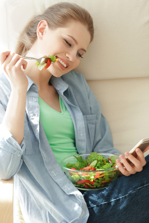 Young woman using mobile phone for counting calories while eating salad. Weight loss conceptの写真素材