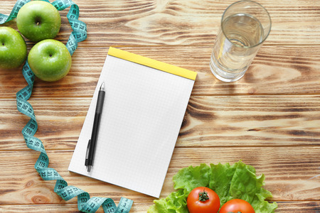 Blank notebook, pen, measuring tape and healthy products on wooden table. Weight loss conceptの写真素材