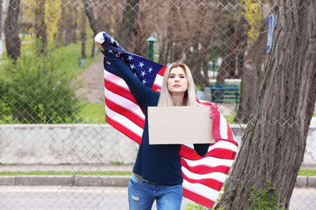 Protesting young woman holding piece of cardboard with space for text and American flag on street