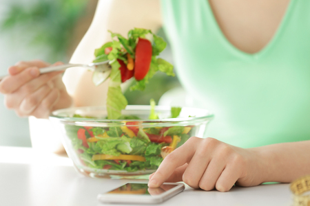 Young woman using mobile phone for counting calories while eating salad, closeup. Weight loss conceptの写真素材