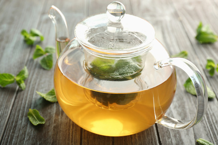 Teapot of hot aromatic tea with lemon balm on wooden tableの写真素材
