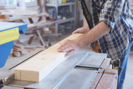 Young carpenter working with circular saw in shop, closeup