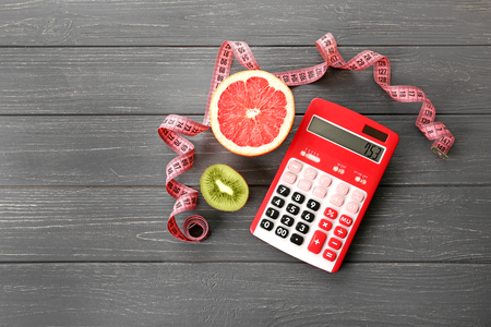 Diet concept. Calculator, measuring tape and grapefruit with kiwi on wooden backgroundの写真素材