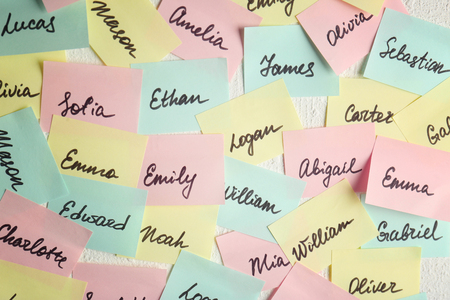 Closeup of paper stickers with different names on white wall. Concept of choosing baby nameの写真素材