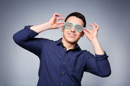 Happy young man with party glasses on gray background