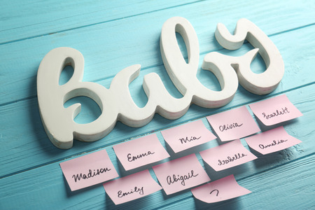 Word BABY and paper stickers with different names on color wooden background. Concept of choosing baby nameの写真素材