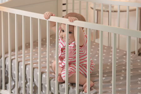 Cute little baby sitting in crib at home