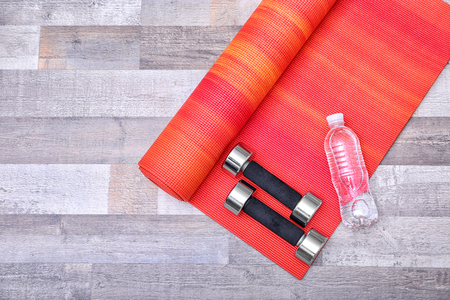 Yoga mat with dumbbells and bottle of water on wooden floorの写真素材