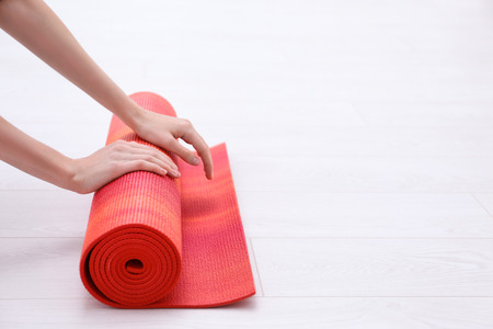 Woman rolling up yoga mat on wooden floorの写真素材