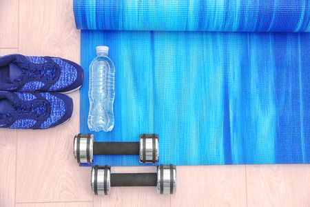 Yoga mat with sneakers, dumbbells, and bottle of water on wooden floorの写真素材